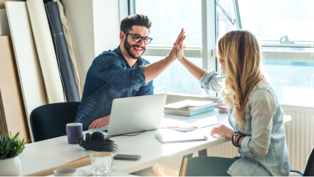 Colleagues high fiving at an office workstation